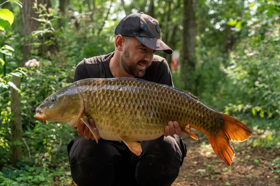 Angler holding a common carp in the woods at Catch 22